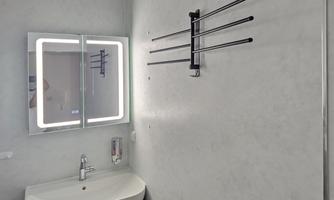 A modern bathroom with a sink and a lit mirror. A towel holder is hanging on the wall.