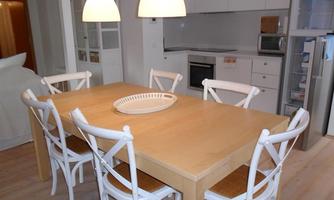 A modern dining area with a large wooden table and six white chairs. The ceiling lights create an inviting atmosphere.