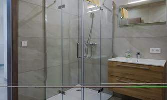A modern bathroom with a glass shower and a wooden sink. The walls are designed with light tiles.