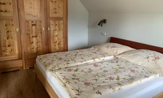 A cozy bedroom with a large double bed and a wooden wardrobe. The bedding has a blooming pattern and the room is bright and friendly.