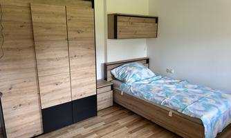 A simple bedroom with a single bed and a wooden wardrobe. The room has a modern and cozy style.
