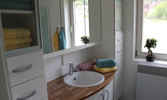 A modern bathroom with a round sink and a wooden countertop. Colorful towels and a small plant create an inviting atmosphere.