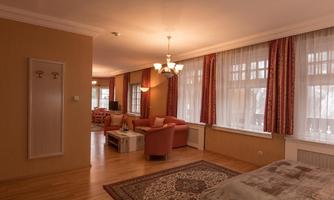 A spacious room with bright walls and large windows. Cozy furniture and a beautiful carpet create an inviting atmosphere.