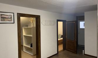 A bright hallway with two open doors. A picture hangs on the wall, and on the other side, there is a shelf.