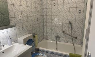 A bathroom with white tiles and a bathtub. There is a sink, a toilet, and a green towel roll.