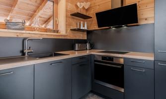 A modern kitchen with dark cabinets and wooden details. It includes a stove, a sink, and a flat-screen TV.