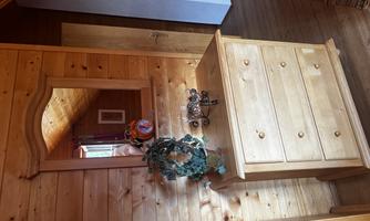A bright wooden dresser stands against a wall with wood paneling. Above the dresser hangs a mirror, while next to it is a beautiful decorative wreath.