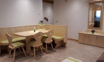 A cozy dining area with a wooden tray and four chairs. The walls are light, and there is a mirror as well as a small decorative plant on the table.