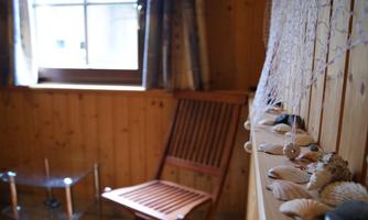 A cozy room with wooden walls and a chair. On the windowsill, there are shells and a glass plate.