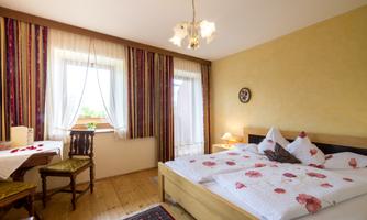 A cozy room with a double bed and a table. The walls are painted in warm colors, and the windows let in plenty of daylight.