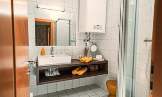 A modern bathroom with a shower and a sink. Towels and hygiene items are neatly arranged on a shelf.