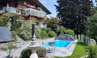 A beautiful house with a balcony full of flowers. The garden has a clear pool and an elegant fountain.