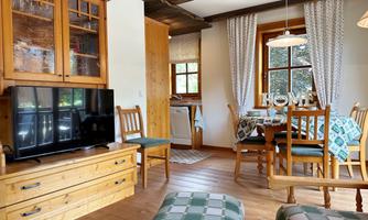 A cozy living room with wooden furniture and a television. The dining area is bright and inviting with a table and chairs.
