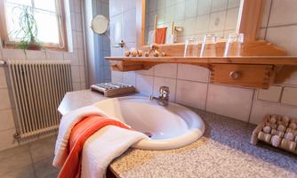 A modern bathroom with a sink and a large mirror. Towels are neatly placed on the shelf and the walls are decorated with bright tiles.