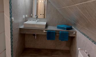 A modern bathroom with a sink and a large mirror. The walls are brightly tiled and there are striking turquoise towels.