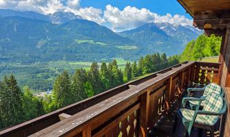 A balcony overlooking impressive mountains and green forests. In the foreground are two chairs, and nature is visibly expansive.
