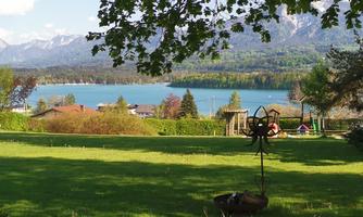 A beautiful view of a lake with a green meadow in the foreground. In the background, mountains and trees are visible.