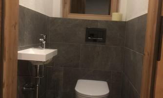 A modern bathroom with gray tiles. There is a wall-mounted toilet and a small sink on the wall.
