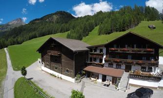 A picturesque country house in the mountains, surrounded by green meadows and trees. The sky is blue with some clouds.