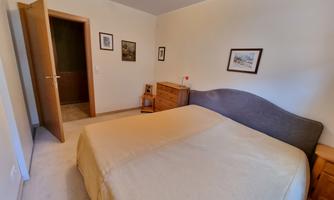 A simple bedroom with a large bed and a beige coverlet. The walls are light and there are some pictures on the walls.
