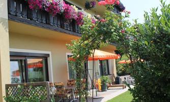 An inviting house with blooming balcony plants and cozy seating in the garden. Sun umbrellas and a green environment create a relaxed atmosphere.