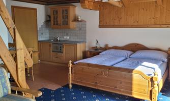 A cozy room with wooden furniture and a double bed. There is a small kitchenette and a dining area.
