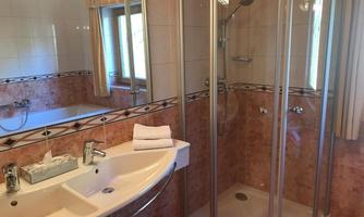 A modern bathroom with a shower and a bathtub. The walls are brightly tiled and the decor is clean and well-maintained.
