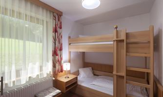 A simple room with bunk beds and a desk. Lots of daylight through the large window.