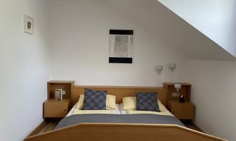 A cozy bedroom with a double bed and navy blue pillows. A picture hangs on the wall, and there are two nightstands with lamps.
