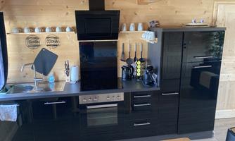 A modern kitchen with black furniture and stainless steel appliances. The kitchen area is set up on a wooden floor in a cozy room.