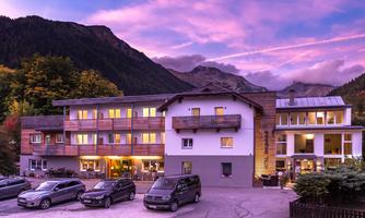 A charming hotel in the mountains with a clear evening sky. In the foreground, parked cars can be seen, surrounded by a picturesque landscape.