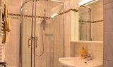 A modern bathroom with a glass shower and a sink. The walls are light-tiled and well-lit.