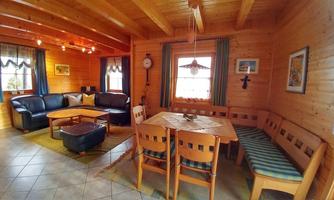 A cozy living space with wooden paneling. There is a sofa, a table, and chairs, surrounded by windows with curtains.