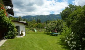A green garden with a lawn and a view of the mountains. In the background, playground equipment and trees can be seen.