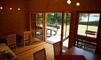 A cozy wooden room with a table and chairs. Large windows offer a view of the garden and the terrace.