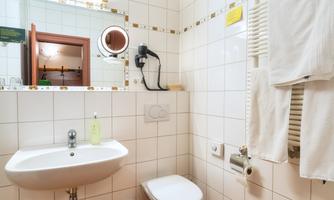 A modern bathroom with white tiles. There is a sink, a toilet, and a wall mirror.