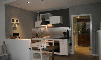 A modern kitchen with a bright color scheme and a small dining area. The furnishings are minimalist and functional.
