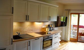 A modern kitchen with white cabinets and an elegant cooktop. In the background, a television and a patio door are visible.