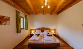 A cozy bedroom with a wooden ceiling and two beds. There are windows with green curtains and soft lighting.