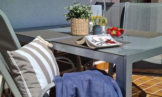 A cozy table on a balcony with a flower pot and fresh strawberries. There is also a blanket and a magazine on the table.