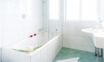 A modern bathroom with a bathtub and a white toilet. The room is bright and features large windows that let in plenty of light.