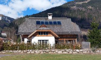 A beautiful, modern house with a traditional roof in a mountain landscape. In the background, green hills and a blue sky can be seen.