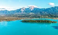 A clear blue lake surrounded by mountains and green islands. The sky is sunny and the landscape is picturesque.
