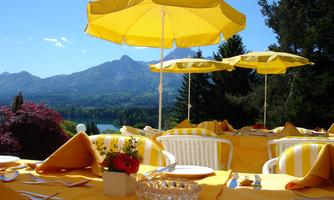 A beautifully set table outdoors with yellow umbrellas and an impressive mountain landscape in the background. The atmosphere is inviting and fresh.