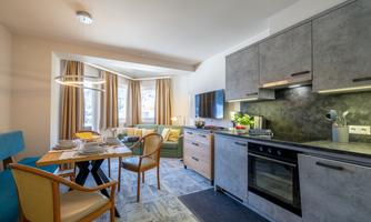 A modern kitchenette with a dining area in a cozy living space. Large windows provide plenty of daylight.