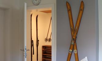 A modern room with bright walls and a wooden floor. Old skis hang on the wall, while a table and chairs are in the foreground.
