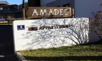A sign with the inscription "AMADEE" and "APPARTEMENTS". It stands in front of a building and is surrounded by grass.