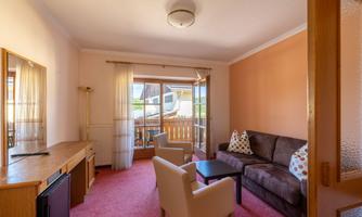 A cozy living room with a sofa and two chairs. Large windows provide a view of the balcony and let in plenty of light.