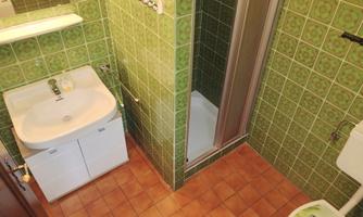 A simple bathroom with green tiles. It contains a sink, a shower, and a toilet.