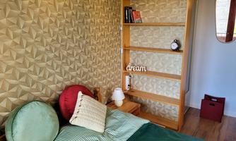 A cozy bedroom with a bed, pillows, and a wooden shelf wall. On the shelf, there is a clock, and the word "dream" is decoratively placed.